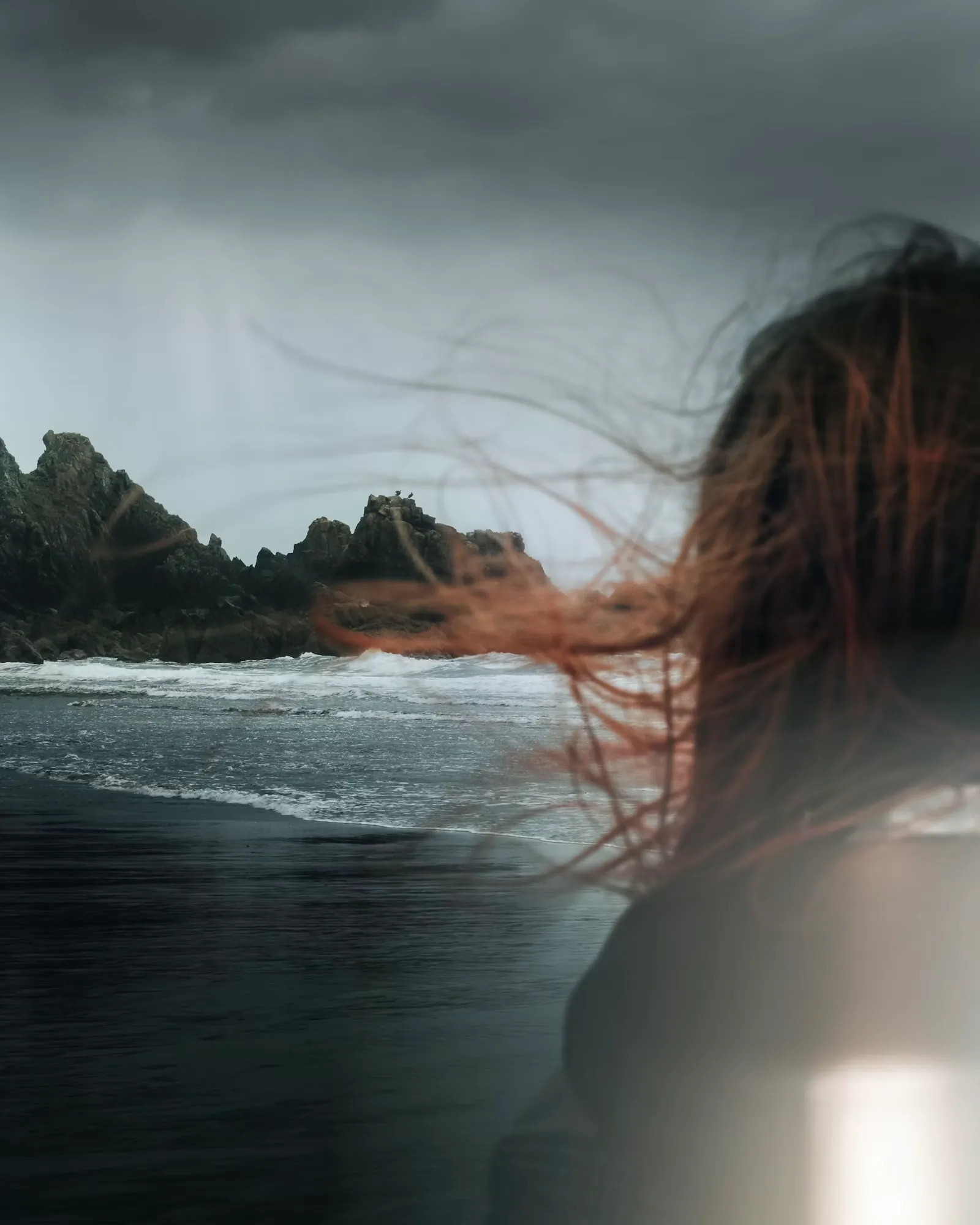 Mujer de pie frente al viento en una playa oscura